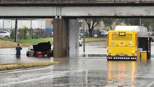 PHOTO: (FILES) In this file photo taken on August 22, 2022 a handout photo provided by the Dallas Police Department shows people standing next to a vehicle sitting in flood waters, along a street in Dallas, Texas. (Handout/Dallas Police Department/AFP )