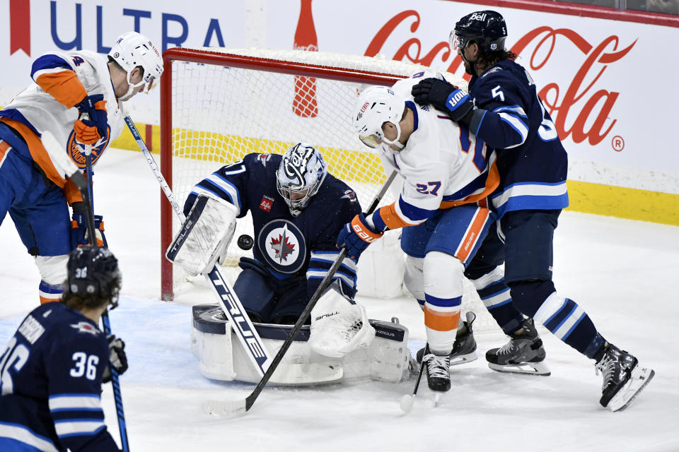 Winnipeg Jets goaltender Connor Hellebuyck (37) makes a save as New York Islanders' Bo Horvat (14) and Anders Lee (27) look for a rebound during the first period of an NHL hockey game Tuesday, Jan. 16, 2024, in Winnipeg, Manitoba. (Fred Greenslade/The Canadian Press via AP)