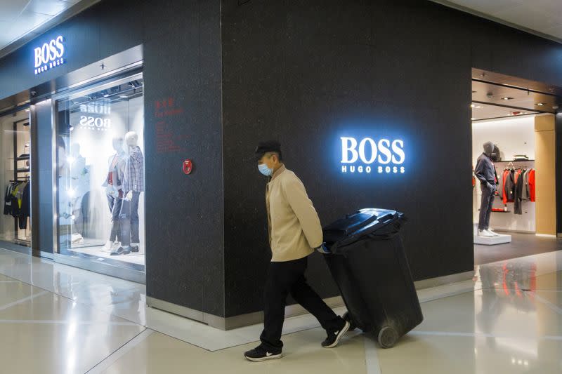 A mall employee pulls a bin past a store of German fashion house Hugo Boss in Beijing