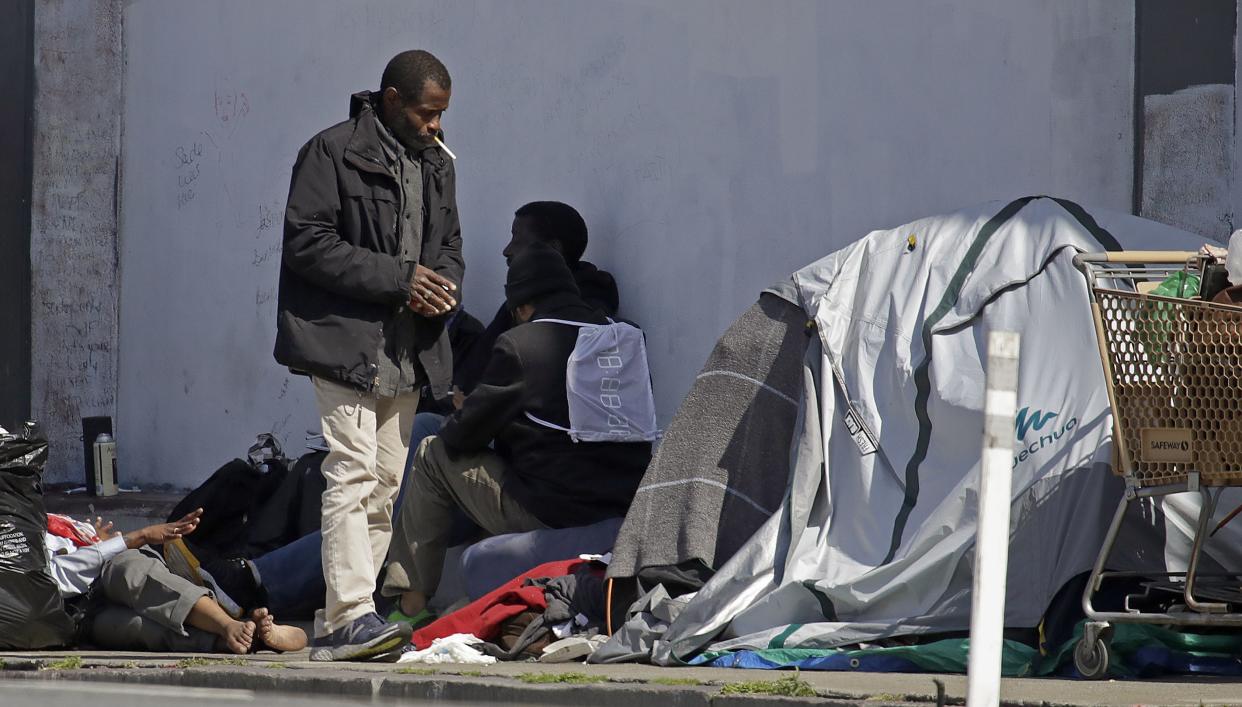 People on the street near the MSC South homeless shelter, where at least 70 people have now tested positive for COVID-19, on Monday, April 13, 2020, in San Francisco, Calif. Local governments have begun moving large numbers of homeless into hotels as part of Operation Roomkey. Among the requirements are that people get tested when they check in and that medical staff at the hotel make regular checks to see if people's conditions change.