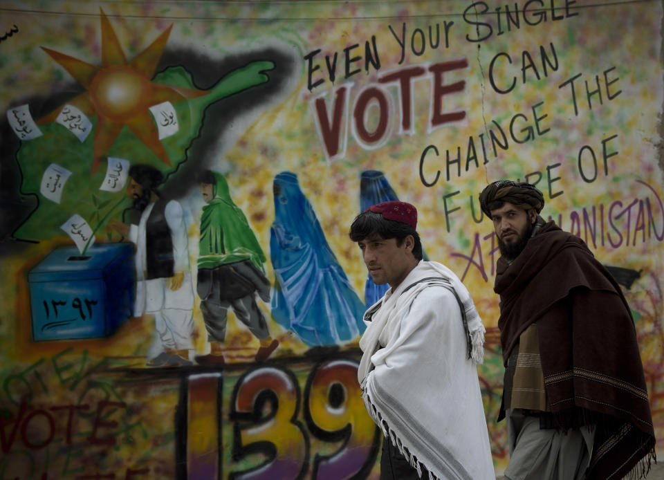 In this Wednesday, March 12, 2014 photo, Afghan men pass an election graffiti demanding people to go to the polls in Kandahar, southern Afghanistan. Warlords with a violent past have played a role in influencing Afghan politics since a U.S.-led coalition helped oust the Taliban in 2001. But they are emerging to play an overt political role in next month’s presidential elections as President Hamid Karzai leaves the scene. (AP Photo/Anja Niedringhaus)