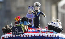 A knitted top cover for a post box depicting Britain's Queen Elizabeth II and her husband Prince Philip in Windsor, England, Friday, April 16, 2021. Prince Philip husband of Britain's Queen Elizabeth II died April 9, aged 99, his funeral will take place Saturday at Windsor Castle in St George's Chapel. The knitted top show some of Prince Philips favorites: the Royal Yacht Britannia, right, the Duke of Edinburgh award scheme for young people and his hobby of carriage driving . (AP Photo/Alastair Grant)