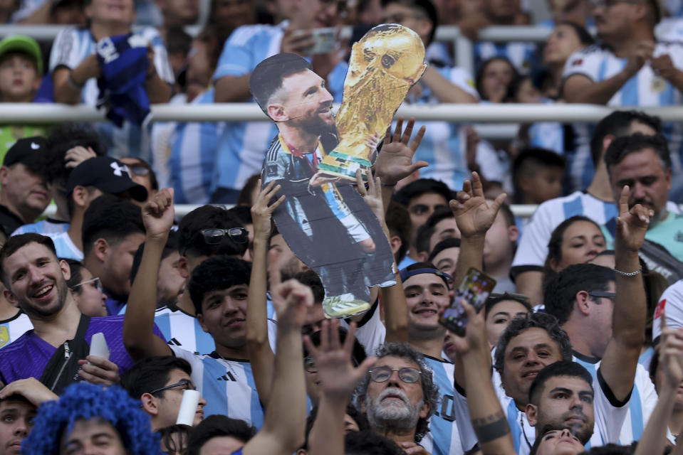 Argentina soccer fans hold a cardboard cutout with the image of soccer star Lionel Messi with the FIFA World Cup trophy as they wait for the start of an international friendly soccer match between Argentina and Curacao in Santiago del Estero, Argentina, Tuesday, March 28, 2023. (AP Photo/Nicolas Aguilera)