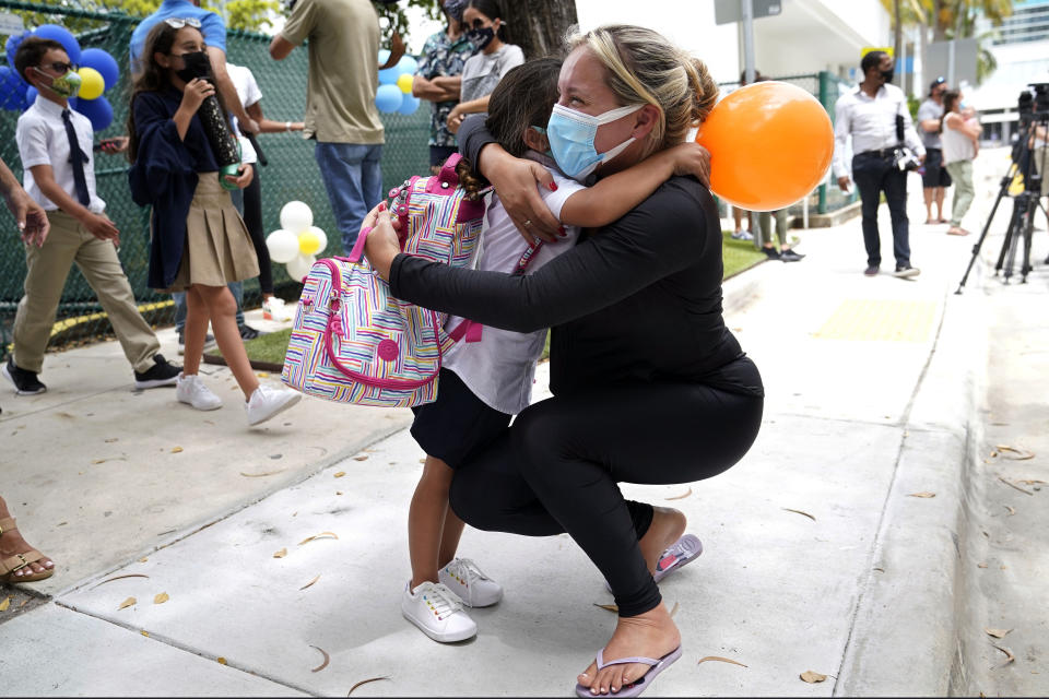 FILE - Carol Basilio, right, hugs her daughter Giovanna outside of iPrep Academy on the first day of school, in Miami, Aug. 23, 2021. In interviews with The Associated Press, close to 50 school leaders, teachers, parents and health officials reflected on decisions to keep students in extended online learning, especially during the spring semester of 2021. (AP Photo/Lynne Sladky, File)