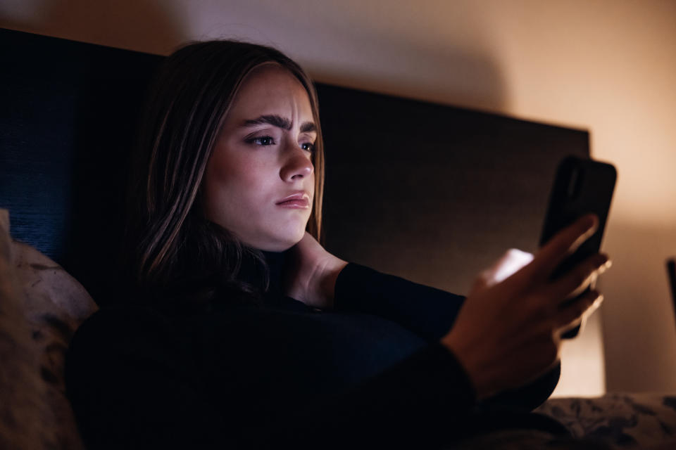 Woman lying in bed looking at her phone with a concerned expression