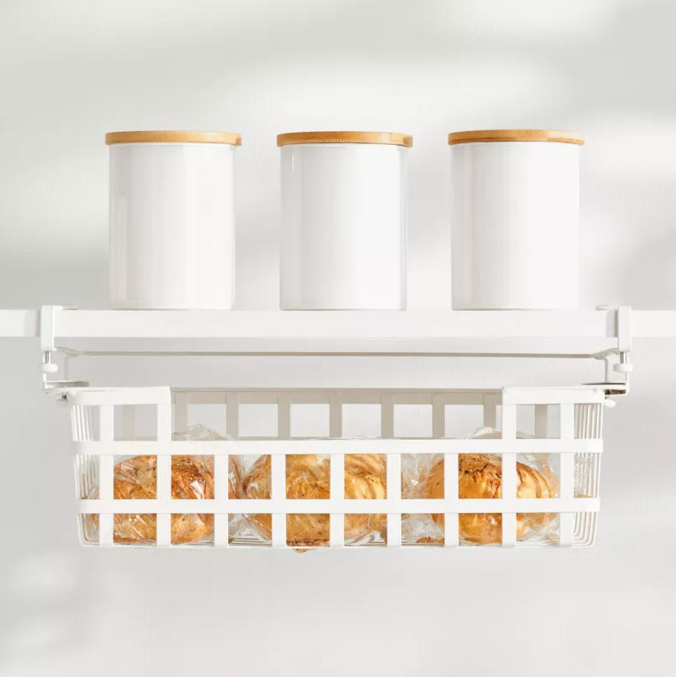 a steel wire basket hanging on a shelf in a white kitchen