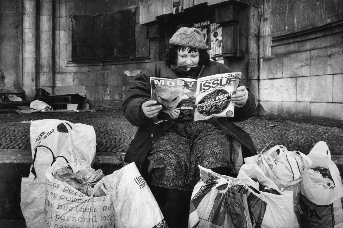 Mary surrounded by her belongings, reading ‘The Big Issue’, in Kingsway, in 1995 (Moyra Peralta/Courtesy of Bishopsgate Institute)