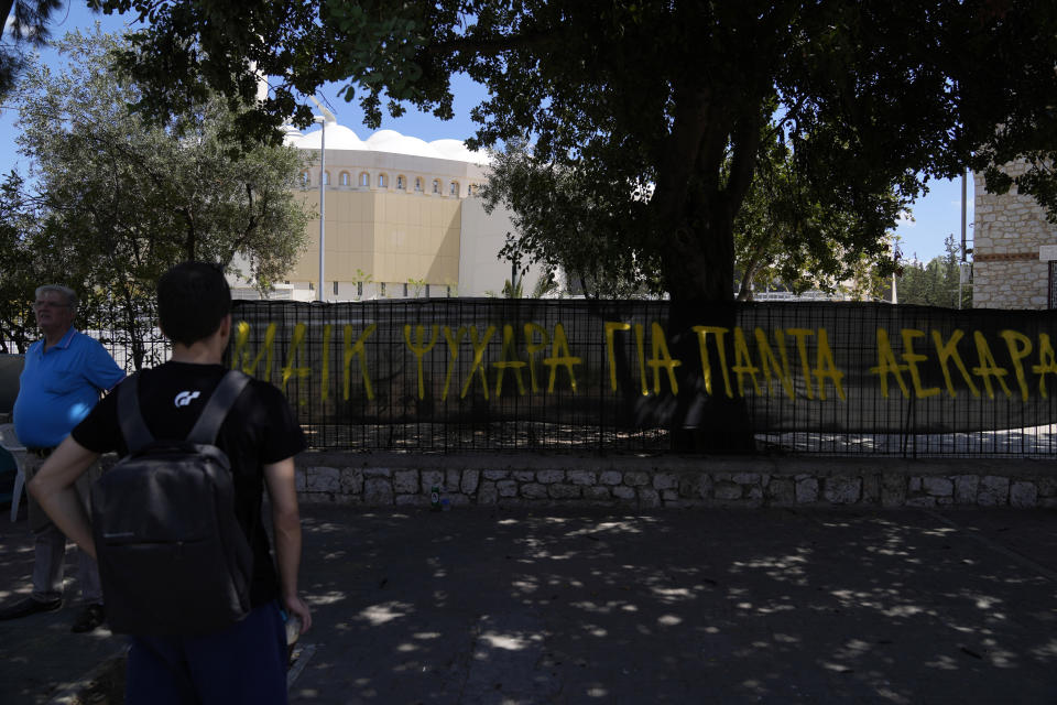 People stand in front of a banner that reads "Big-hearted Mike, AEK forever" outside OPAP Arena, in Nea Philadelphia suburb, in Athens, Greece, Tuesday, Aug. 8, 2023. A 29-year-old fan was killed in overnight clashes between rival supporters in the Greek capital, prompting European governing soccer body UEFA to postpone a Champions League qualifying game between AEK Athens and Croatia’s Dinamo Zagreb on Tuesday. (AP Photo/Thanassis Stavrakis)