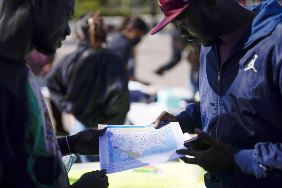 Two migrants study a map of the United States in a parking lot set up to help people with travel plans, accommodation, food and shelter, Friday, Oct. 6, 2023, in San Diego. San Diego's well-oiled system of migrant shelters is being tested like never before as U.S. Customs and Border Protection releases migrants to the streets of California's second-largest city because shelters are full. (AP Photo/Gregory Bull)