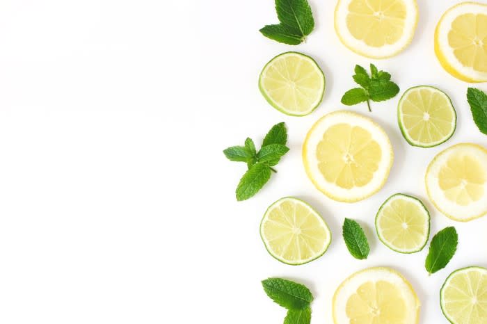 Sliced lemons and limes artfully arranged with mint leaves on a white table.