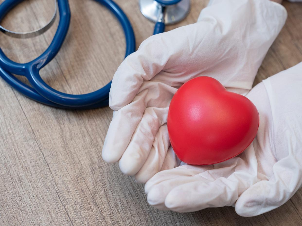 Doctor wearing surgical gloves holding red heart with a stethoscope.