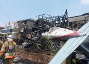 The tail section of a crashed light plane (R) and burning house are seen after the plane went down in a residential area and burst into flames, in Chofu, outskirt of Tokyo, in this photo taken by Kyodo July 26, 2015. (REUTERS/Kyodo)