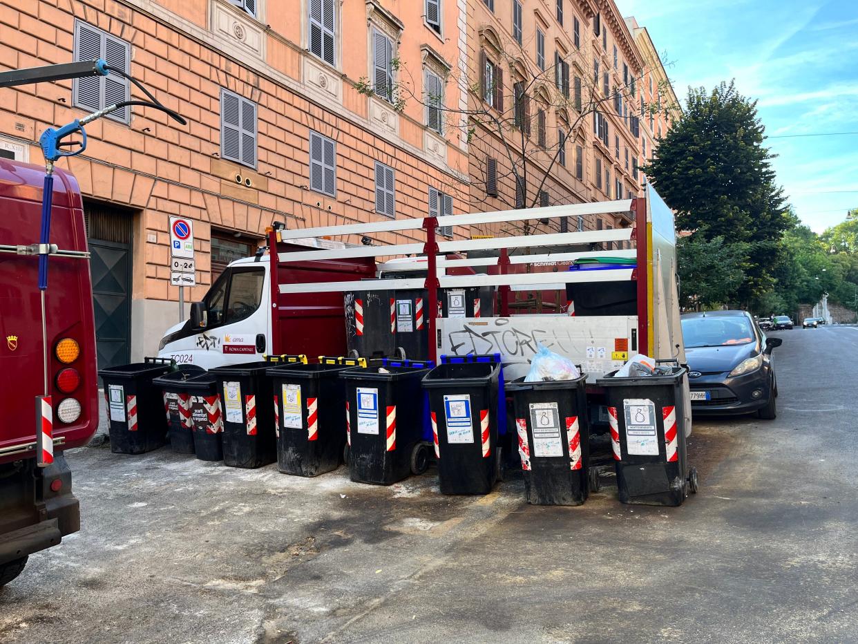 A line of trash cans behind a building in Italy