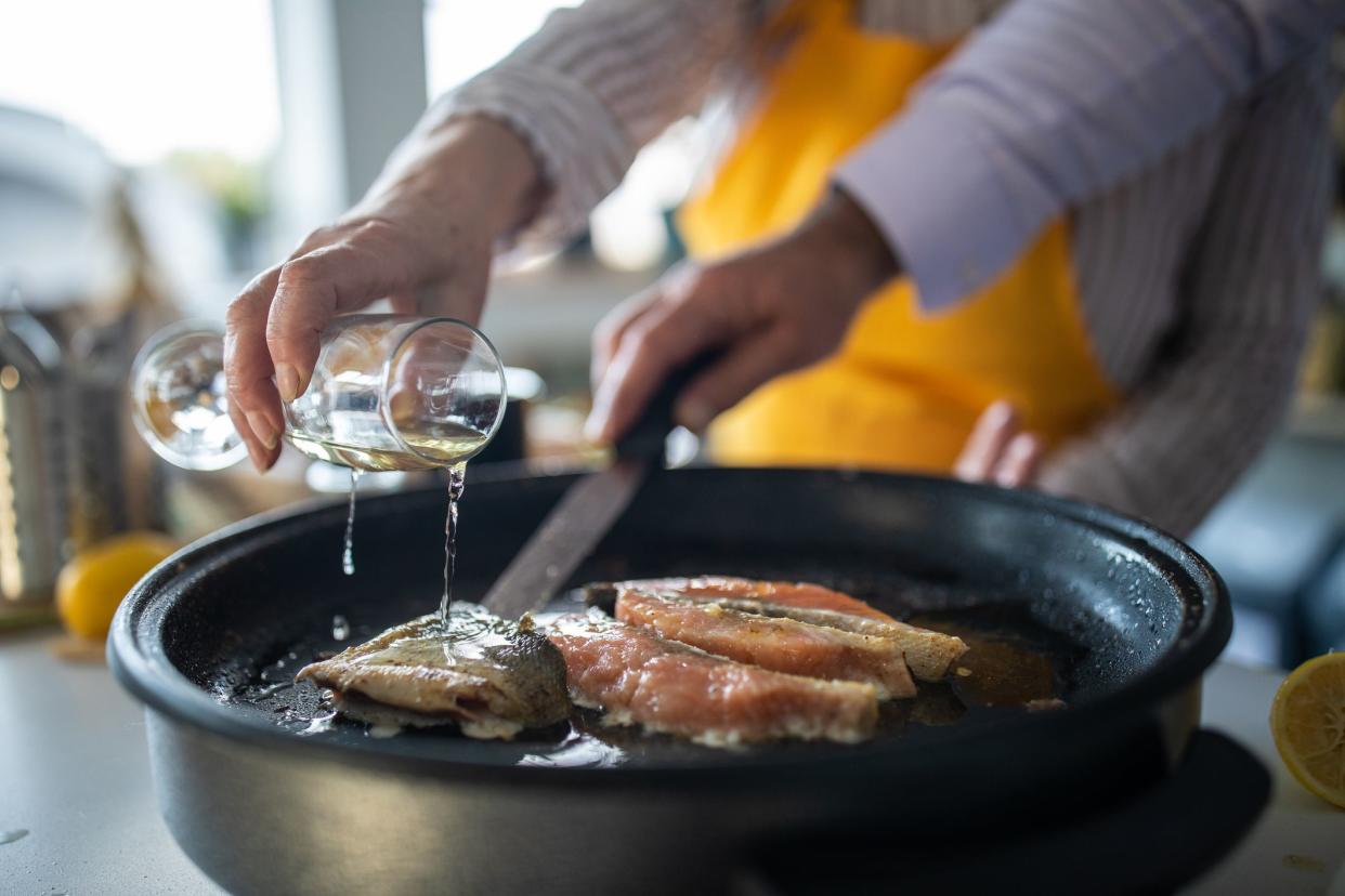 Senior woman adding white wine while preparing fish with her husband at home