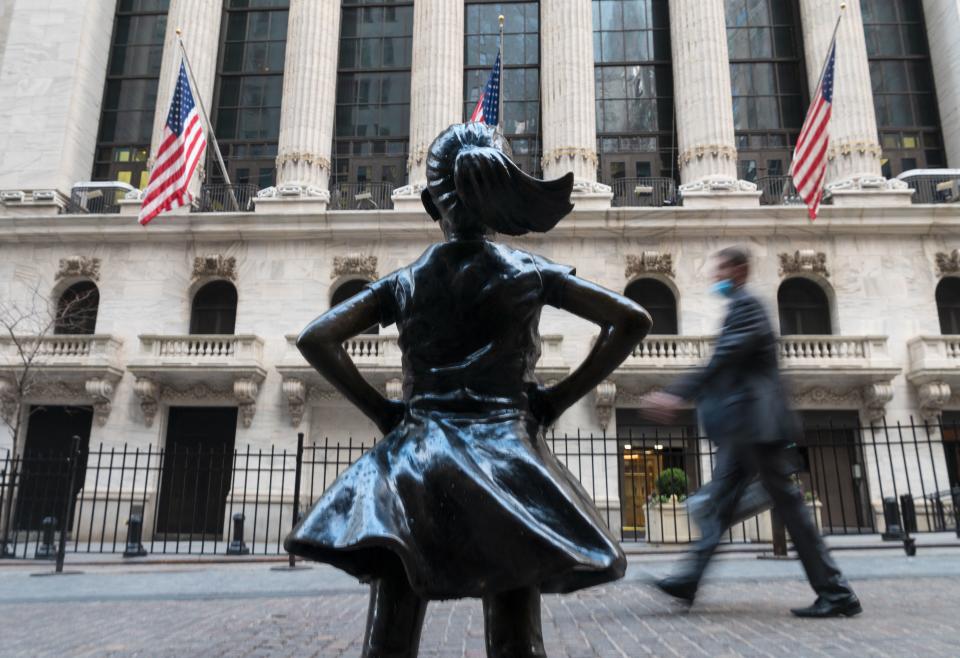 People walk past the New York Stock Exchange (NYSE) at Wall Street and the  'Fearless Girl' statue on March 23, 2021 in New York City. - Wall Street stocks were under pressure early ahead of congressional testimony from Federal Reserve Chief Jerome Powell as US Treasury bond yields continued to retreat. (Photo by Angela Weiss / AFP) (Photo by ANGELA WEISS/AFP via Getty Images)