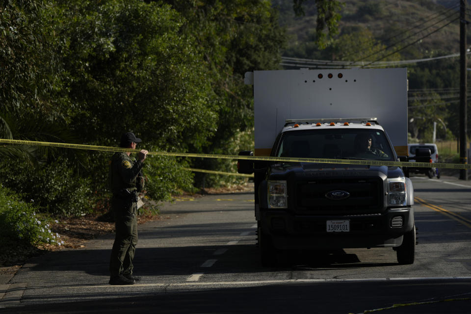 CAPTION CORRECTION: CORRECTS NAME OF BAR: A member of the Orange County Sheriffs Dept. left, lifts police tape for law enforcement vehicles to go through at the scene of a mass shooting near Cook's Corner, Thursday, Aug. 24, 2023, in Trabuco Canyon, Calif. Gunfire at a popular Southern California biker bar killed three people and wounded several others Wednesday, and the gunman — believed to be a retired law enforcement officer — was fatally shot by deputies, authorities said. (AP Photo/Jae C. Hong)