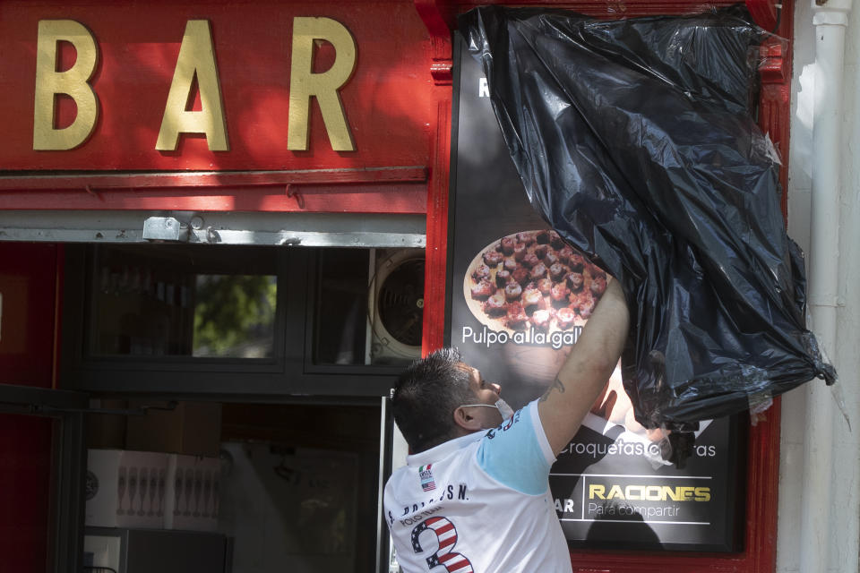 A worker uncovers the front of a bar ready to open for the first time in over two months in Madrid, Spain, Monday, May 25, 2020. Spain is making progress on its staggered plan out of the confinement against the coronavirus. Roughly half of the population, including residents in the biggest cities of Madrid and Barcelona, enters phase 1, Monday which allows for social gatherings in limited numbers, restaurant and bar services with outdoor sitting and some cultural and sports activities. (AP Photo/Paul White)