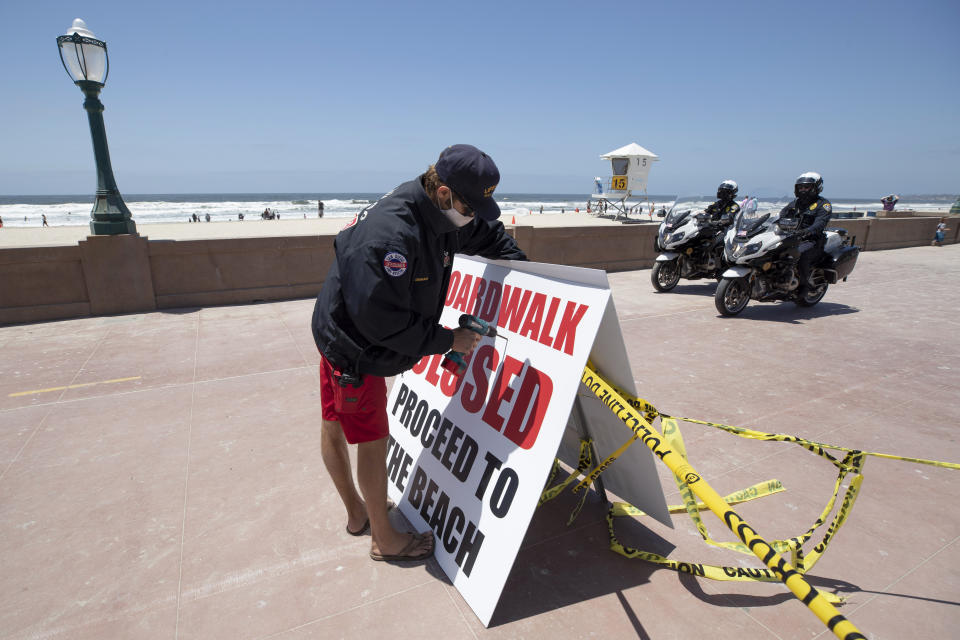 A San Diego lifeguard posts a sign along the closed beachfront boardwalk Friday, May 22, 2020, in San Diego. Millions of Californians are heading into the Memorial Day weekend with both excitement and anxiety after restrictions to control the spread of coronavirus were eased across much of the state. (AP Photo/Gregory Bull)