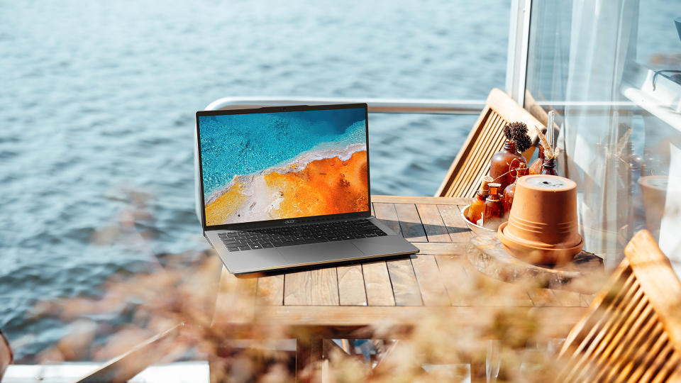 Imagen de marketing de estilo de vida del Acer Swift Go 14 sentado en una mesa al aire libre junto a la playa.