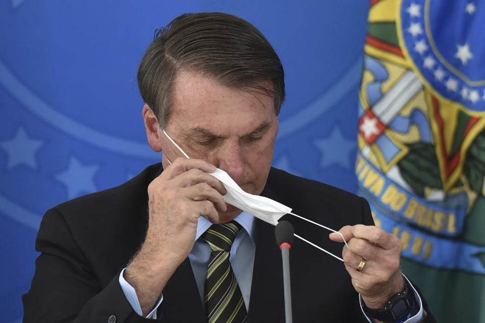 Brazil's President Jair Bolsonaro awkwardly puts on a mask during a March 18 press conference. (Photo: Andre Borges/ASSOCIATED PRESS)