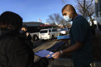 Pharmacy technician, Luis Garcia, passes out forms to people waiting for COVID-19 tests outside Asthenis Pharmacy in Providence, R.I., Tuesday, Dec. 7, 2021. Even as the U.S. reaches a COVID-19 milestone of roughly 200 million fully-vaccinated people, infections and hospitalizations are spiking, including in highly-vaccinated pockets of the country like New England. (AP Photo/David Goldman)