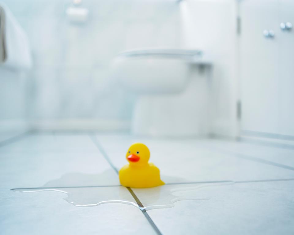 Gleaming white, tiled bathroom floor with yellow rubber duck sitting in the middle, in focus