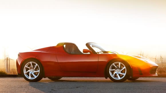 Red convertible on road in desert landscape near sunset or sunrise.