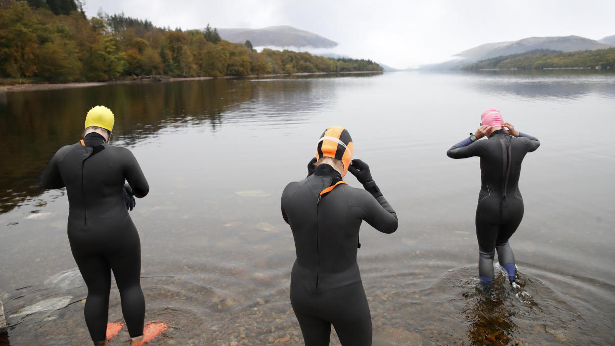  Open water swimmers wearing wetsuits getting ready to go swimming in a Scottish loch. 