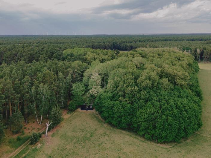 A Raus cabin in nature surrounded by trees and open fields.