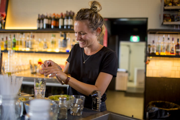 A female bartender squeezes lime into a drink behind a bar.