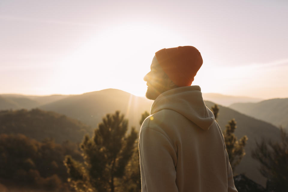 A young man standing outside by a sunset feeling mindful. (Photo via Getty Images)