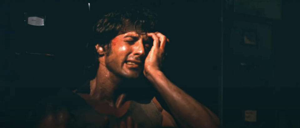 Sylvester Stallone, drenched in sweat, grimaces and holds his head in a dramatic scene