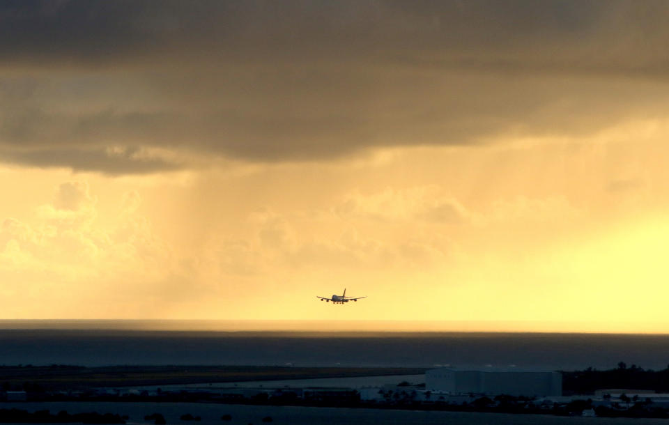 FILE - In this April 6, 2020 file photo, a plane lands as the sun sets over the Pacific Ocean in Honolulu. The small, tight-knit community of about 72,000 people on the neighboring Hawaiian island of Kauai spent the first seven months of the pandemic mostly COVID-free. Then in October, statewide travel restrictions eased and the island, which had only 61 known cases of coronavirus from March through September, went from zero cases in October to at least 84 new infections in just seven weeks. (AP Photo/Caleb Jones, File)