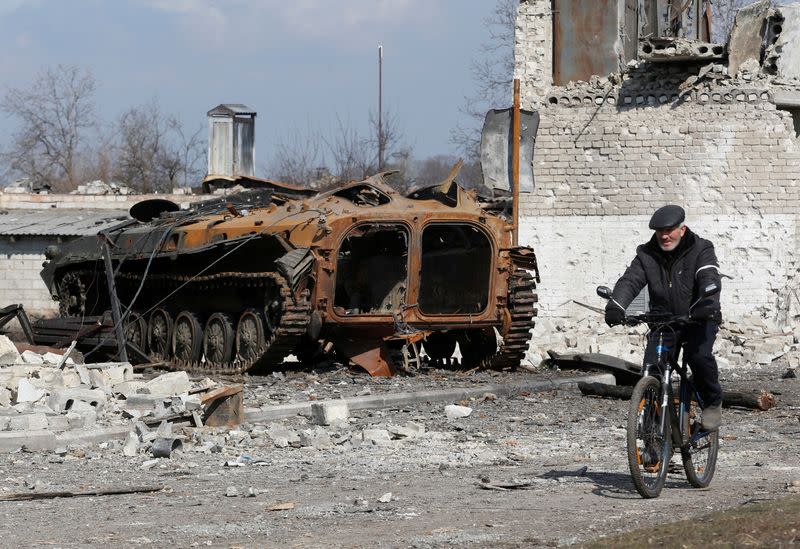 FILE PHOTO: A local resident rides a bicycle past a charred armoured vehicle in Volnovakha