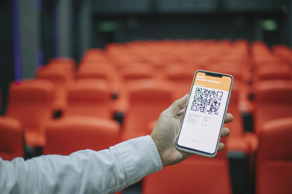 Person holding phone with a QR code displayed on the screen in an empty theater with orange seats