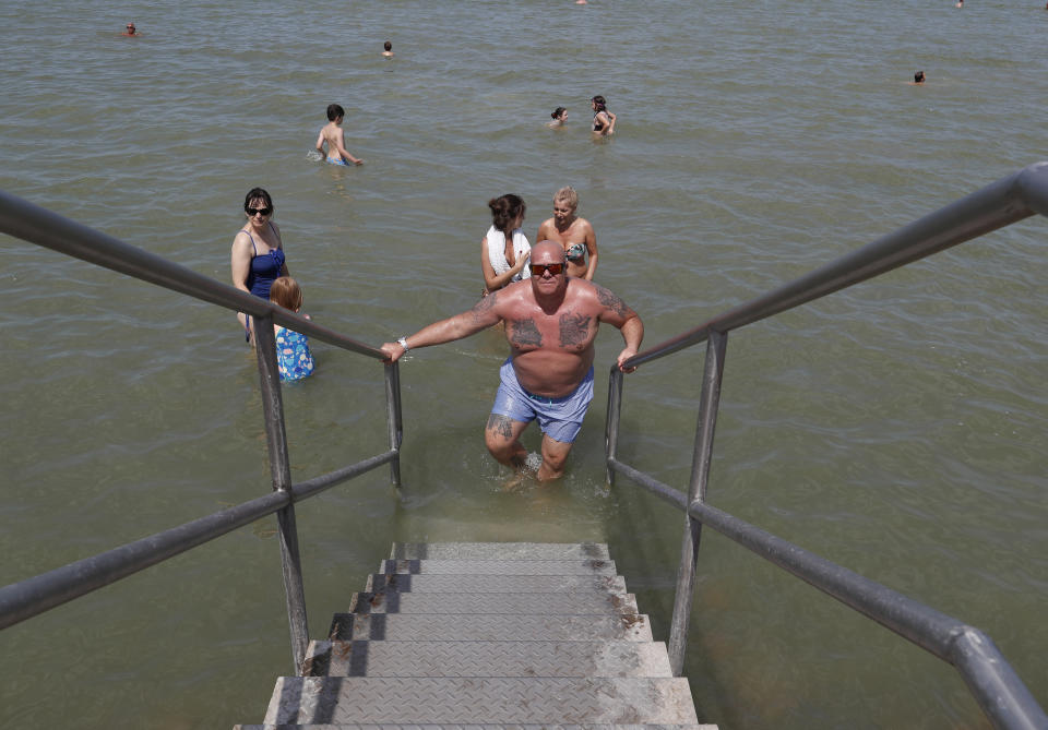 A man walks out from the Lake Velence in Agard, Hungary, Sunday, Aug. 8, 2021. Activists and environmental experts in Hungary say the effects of climate change and insufficient infrastructure are colliding to threaten the country’s third largest natural lake with an economic and ecological crisis. Lake Velence has lost nearly half of its water in the last two years as hot, dry summers have led to increased evaporation and deteriorating water quality. (AP Photo/Laszlo Balogh)