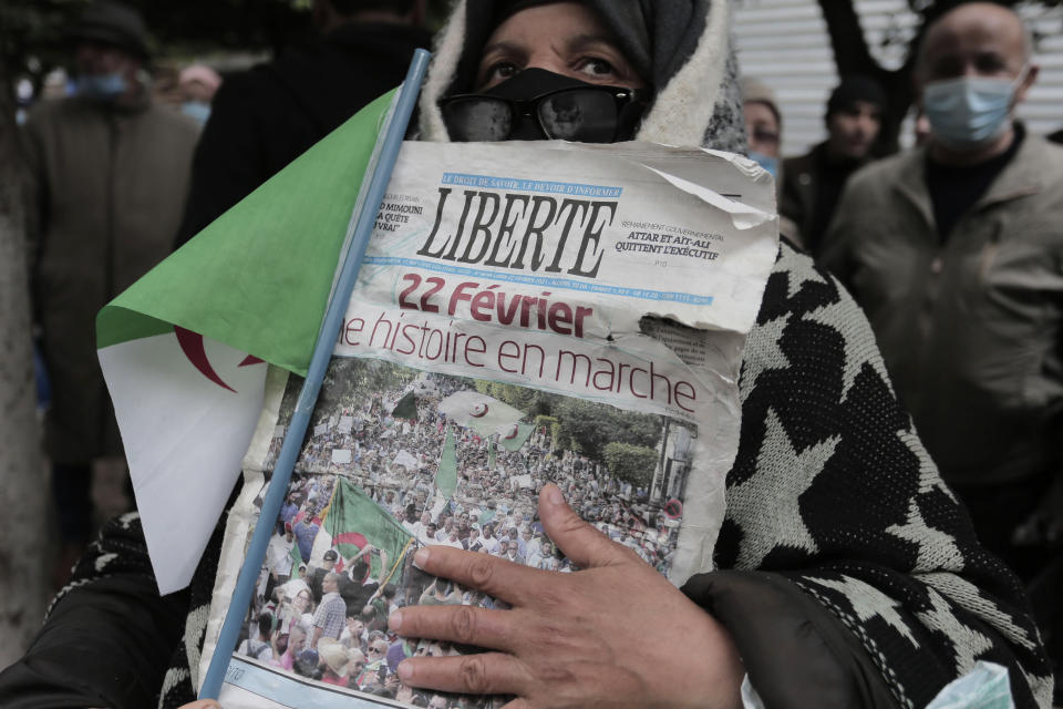 A woman holds a newspaper headlining "Feb.22, History coming" as Algerians demonstrate in Algiers to mark the second anniversary of the Hirak movement, Monday Feb. 22, 2021. Thousands of protesters marking the second anniversary of Algeria's pro-democracy movement took to the streets Monday in the Algerian capital where a wall of security forces stepped aside to let marchers pass. (AP Photo/Toufik Doudou)