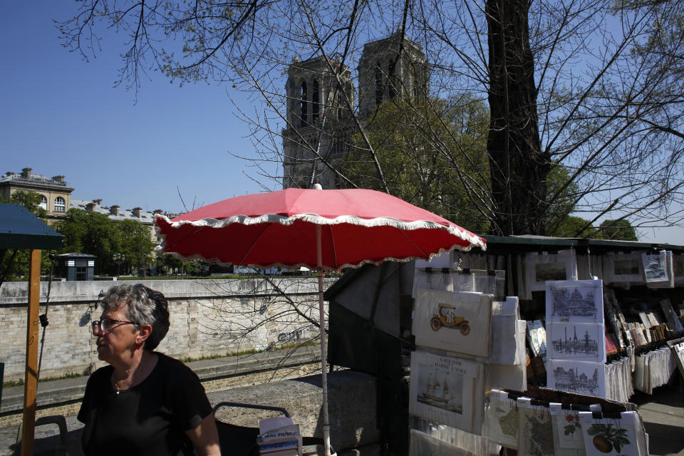 A book seller stands near Notre Dame cathedral, in Paris, Friday, April 19, 2019. Rebuilding Notre Dame, the 800-year-old Paris cathedral devastated by fire this week, will cost billions of dollars as architects, historians and artisans work to preserve the medieval landmark. (AP Photo/Thibault Camus)