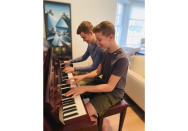 This Nov. 20, 2020 photo released by Andrea Fage shows brothers Rafael Fage, 16, background, ad Noah Fage, 14 playing the piano at their home in Harrison, N.Y. During the pandemic lockdown, private piano lessons for boys stopped. They researched movie soundtracks and learned the score on their own with the assistance of sites like YouTube. (Andrea Fage via AP)