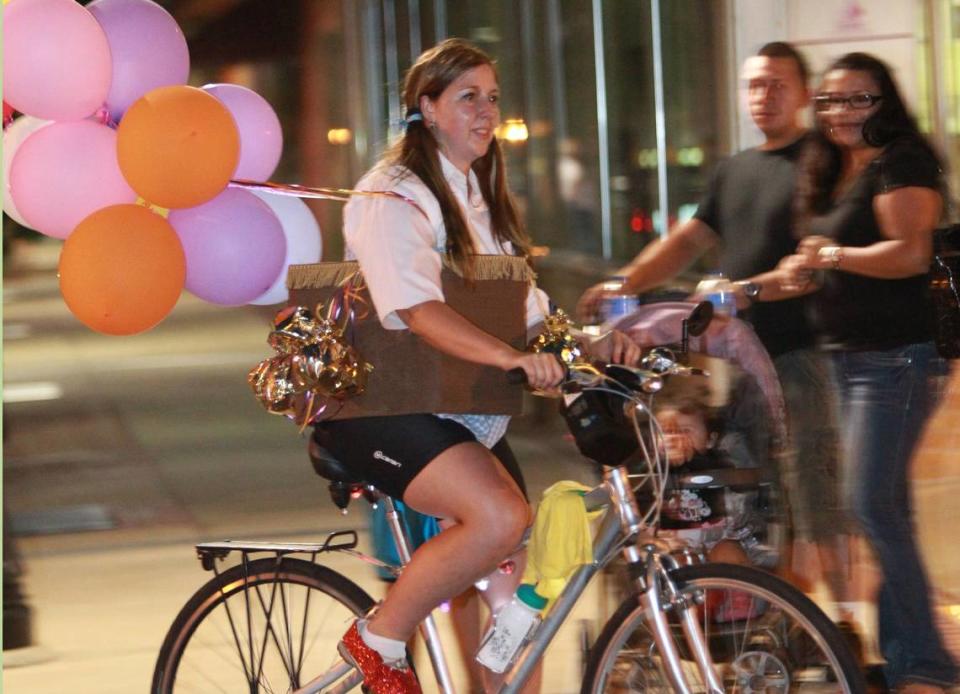 Tara Renneke wears a Dorothy costume with ruby slippers on a bicycle with balloons.