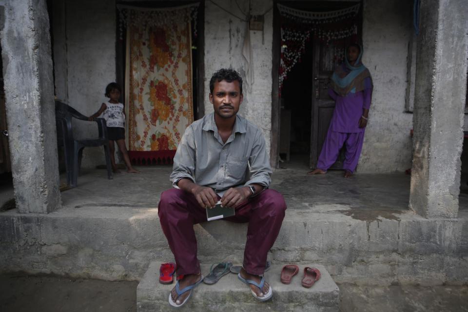 In this Nov. 23, 2016 photo, Mohammed Tohit, 28, holds his passport in front of the solid, cement and plaster home that he built for his family in Belhi Village, Nepal. Tohit is the envy and inspiration of the village. He worked in Malaysia for almost six years sewing clothes for Nike, Lacoste and Columbia Sportswear, saving more than $20,000, enough to build the sturdy two-bedroom house. "I am scared, sure, but I have no way to earn anything here," he says. "I have no choice but to leave again." (AP Photo/Niranjan Shrestha)