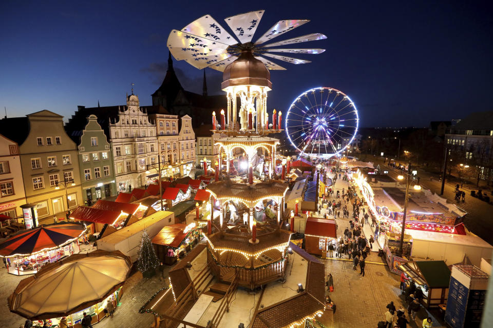 FILE - People visit the illuminated Christmas Market in Rostock, Germany, Monday, Nov. 22, 2021. Despite the pandemic inconveniences, stall owners selling ornaments, roasted chestnuts and other holiday-themed items in Frankfurt and other European cities are relieved to be open at all for their first Christmas market in two years, especially with new restrictions taking effect in Germany, Austria and other countries as COVID-19 infections hit record highs. (Bernd Wuestneck/dpa via AP, File)