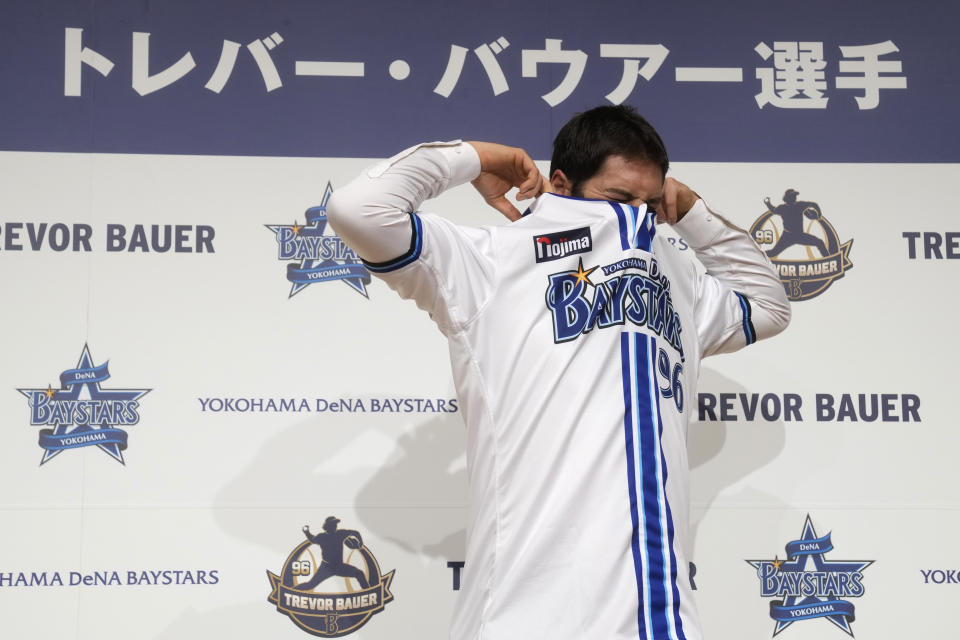 Trevor Bauer puts on his new uniform of Yokohama DeNA BayStars during a photo session of the news conference Friday, March 24, 2023, in Yokohama, near Tokyo. (AP Photo/Eugene Hoshiko)