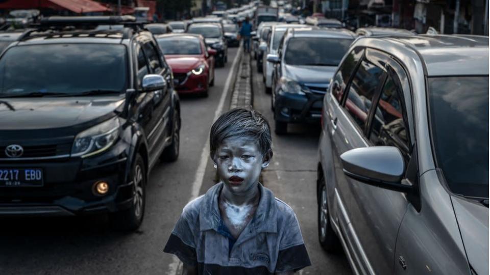 Garoto indon&#xe9;sio com pele pintada de prata anda entre carros em uma rodovia congestionada