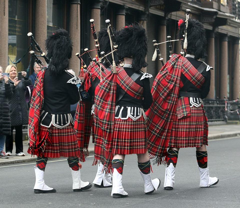 Bagpipe players walk down a street