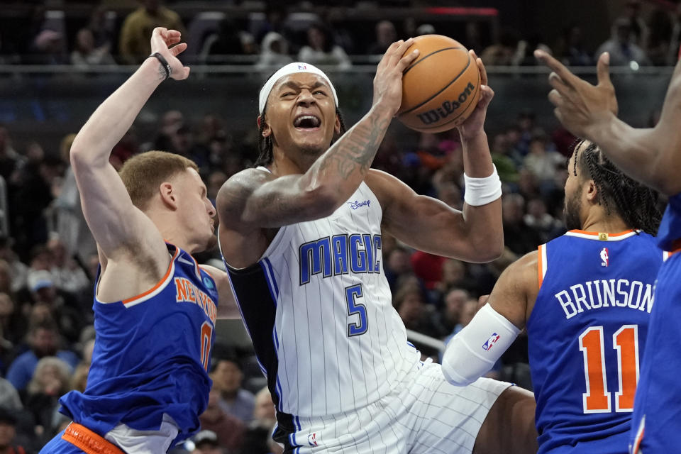 Orlando Magic forward Paolo Banchero (5) goes up to shoot between New York Knicks guards Donte DiVincenzo, left, and Jalen Brunson (11) during the second half of an NBA basketball game, Friday, Dec. 29, 2023, in Orlando, Fla. (AP Photo/John Raoux)