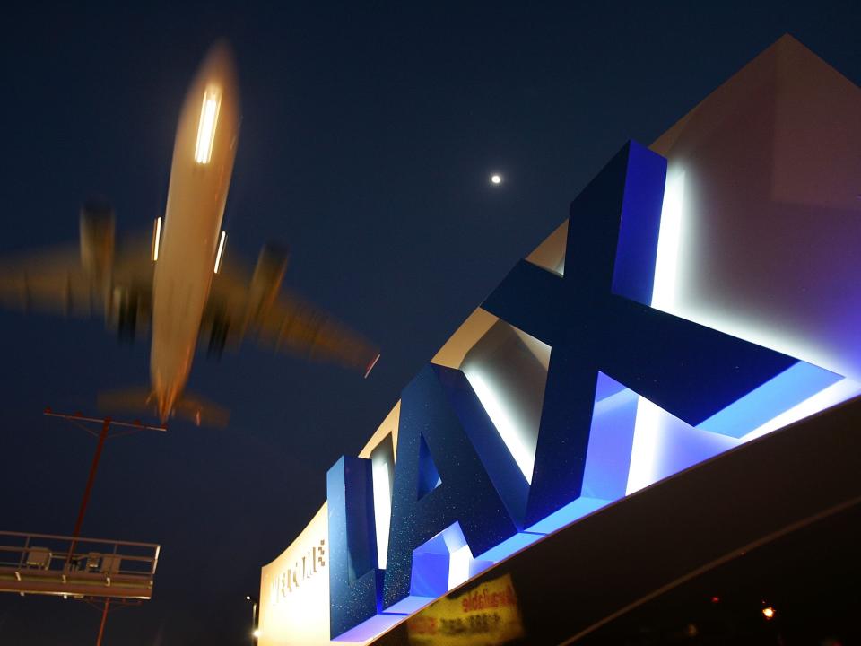 A nighttime view of the LAX sign lit up while a blurry plane flies by overhead.