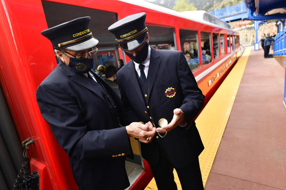 Conductors David Bolser, left, and Adam Clawson, right, check the time on their pocket watches as they helps get passengers aboard The Broadmoor Manitou and Pikes Peak Cog Railway train in May 2021.  / Credit: Helen H. Richardson/MediaNews Group/The Denver Post via Getty Images