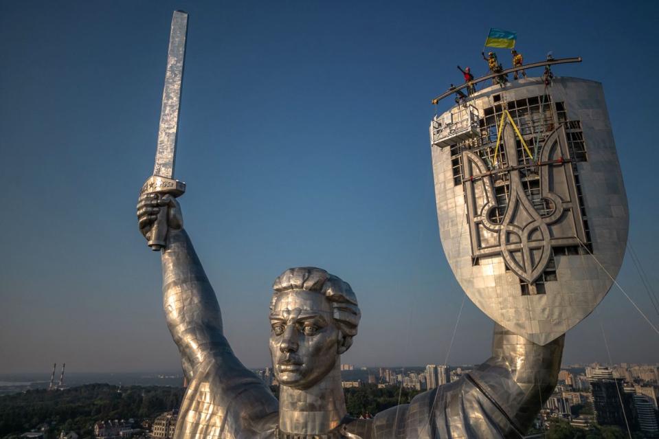 This aerial view taken on Aug. 6, 2023, shows steeplejacks installing the coat of arms of Ukraine on the shield of the 62-meter Motherland Monument in Kyiv, amid the Russian invasion of Ukraine. The Ukrainian trident replaced the coat of arms of the former Soviet Union, which was removed earlier in August 2023. (Roman Pilipey/AFP via Getty Images)