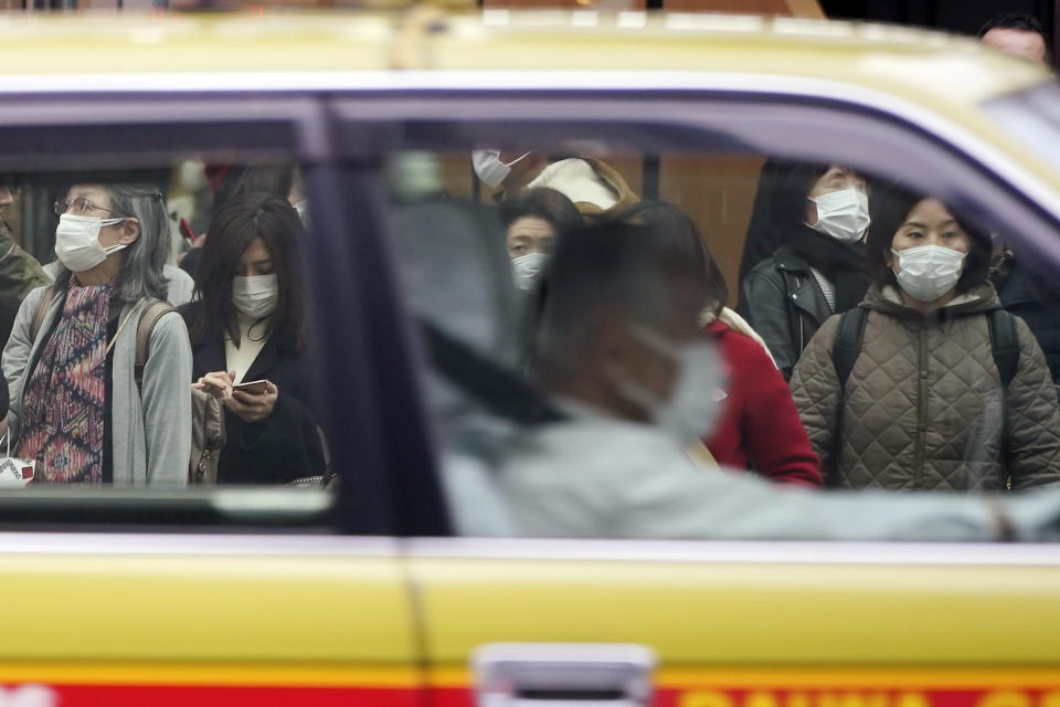 A taxi drives past pedestrians wearing masks as they wait at traffic light in Ginza shopping district Wednesday, Feb. 26, 2020, in Tokyo. At a government task force meeting Wednesday on the virus outbreak, Prime Minister Abe said he was asking organizers to cancel or postpone major sports or cultural events over the next two weeks. (AP Photo/Eugene Hoshiko)